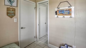 A hallway with a door, a framed sign on the wall, and a basket of towels. - Oceanfront Ormond Beach Getaway w/ Balcony! (Ormond Beach)