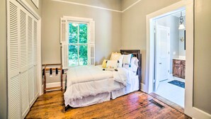 Une chambre à coucher avec un lit, une fenêtre avec des volets, un plancher en bois et une porte donnant sur une autre pièce.