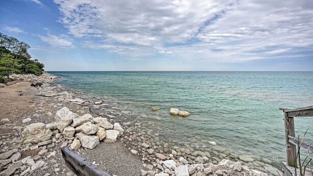 A rocky shoreline with clear water and a wooden structure. - Lake Michigan Hideaway: Pool, Steps to Beach! (New Buffalo)
