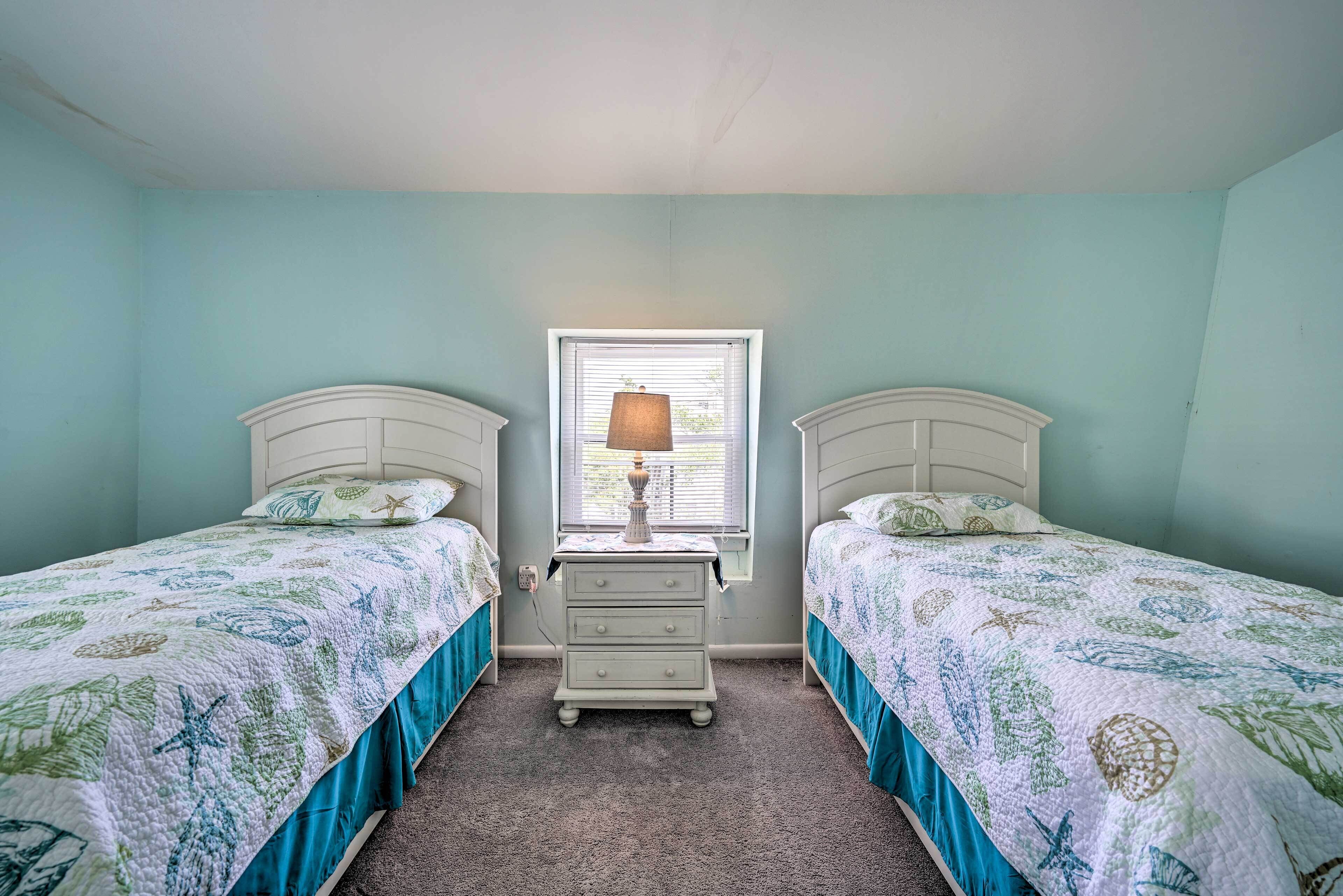 A bedroom with two beds, a nightstand, and a window with blinds.