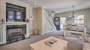 A living room with a fireplace, a staircase, a dining area, and a view of the outside. - Charming Ocean City Townhome: Walk to Beach! (Ocean City)