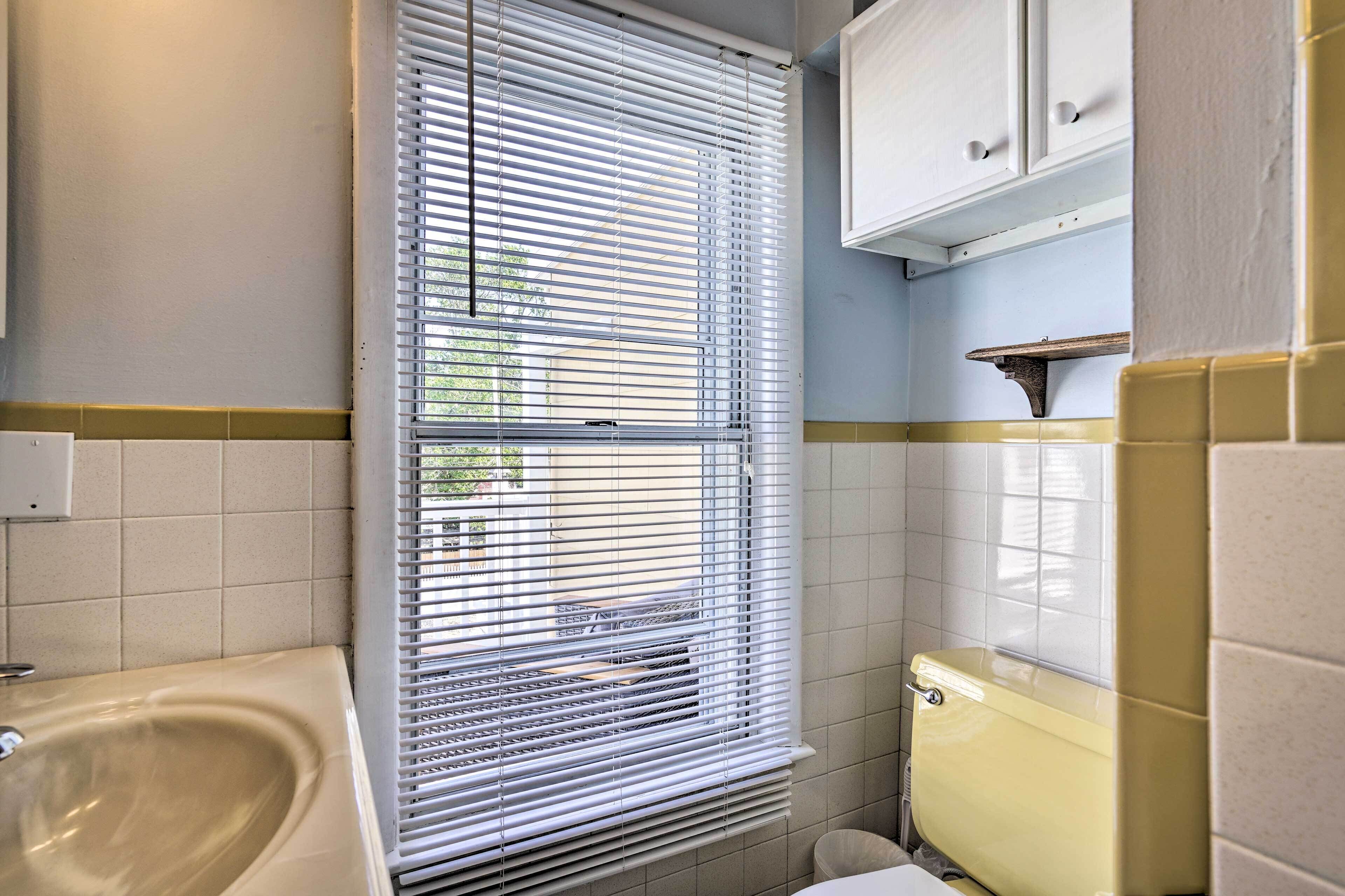 A bathroom with a bathtub, toilet, and window with blinds.