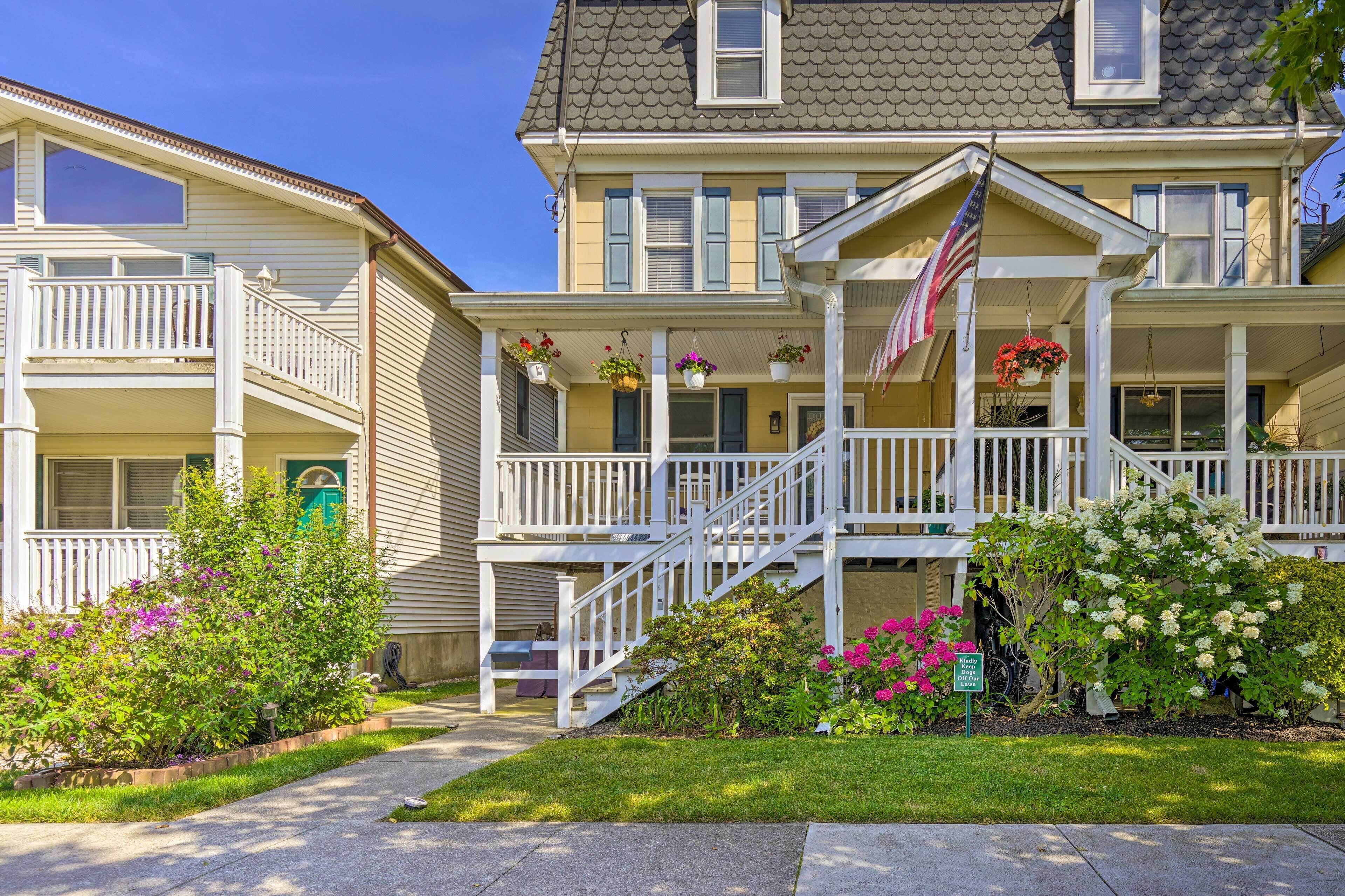 Ein zweistöckiges Haus mit Veranda, Treppe und einem kleinen Garten mit Blumen.