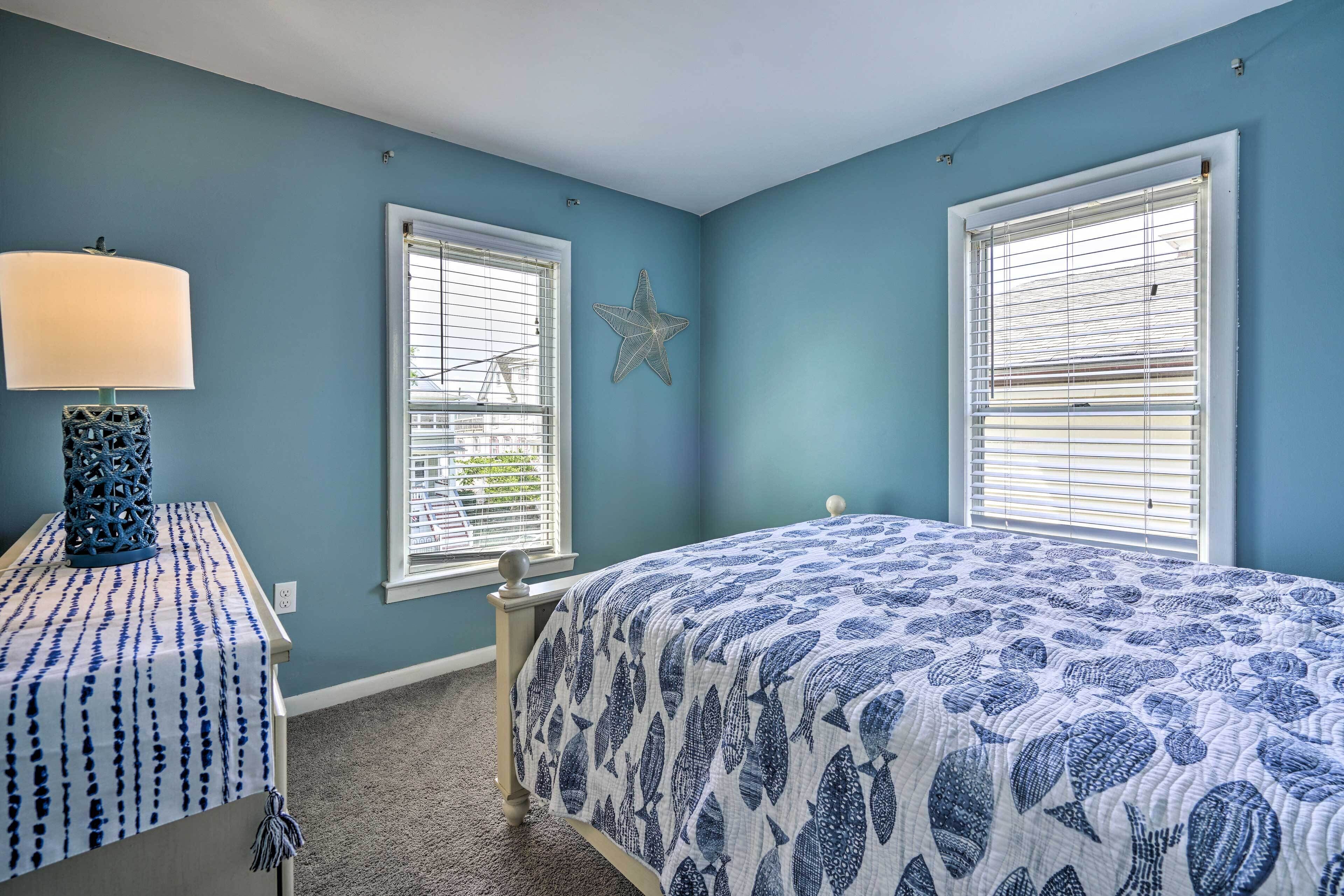 Un dormitorio con una cama, dos ventanas, una decoración de estrellas y una lámpara en una mesita de noche.