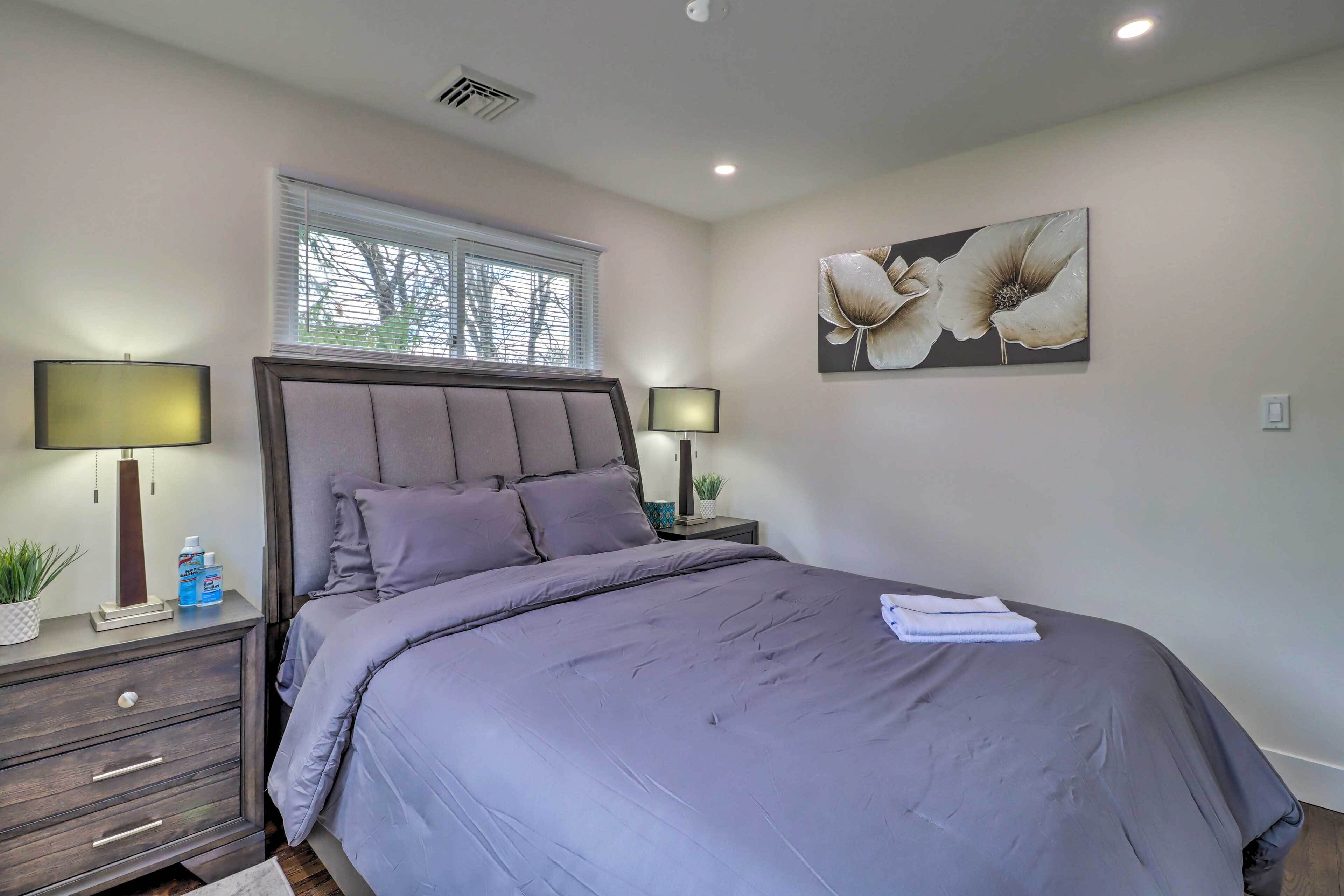 Une chambre avec un grand lit, deux tables de chevet avec des lampes, une fenêtre avec des stores et un tableau floral accroché au mur.