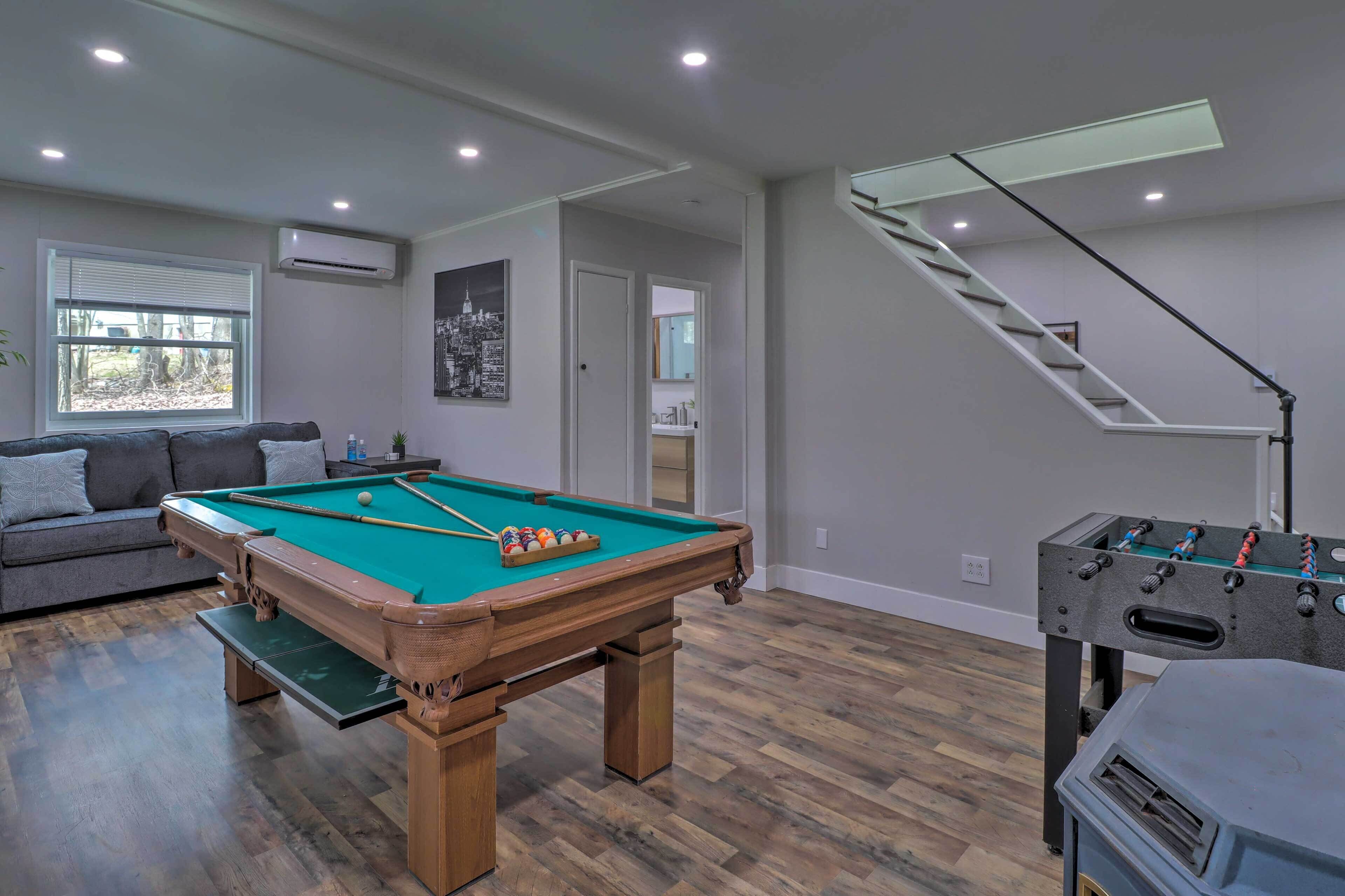 A living room with a pool table, a sofa, a foosball table, and a staircase.