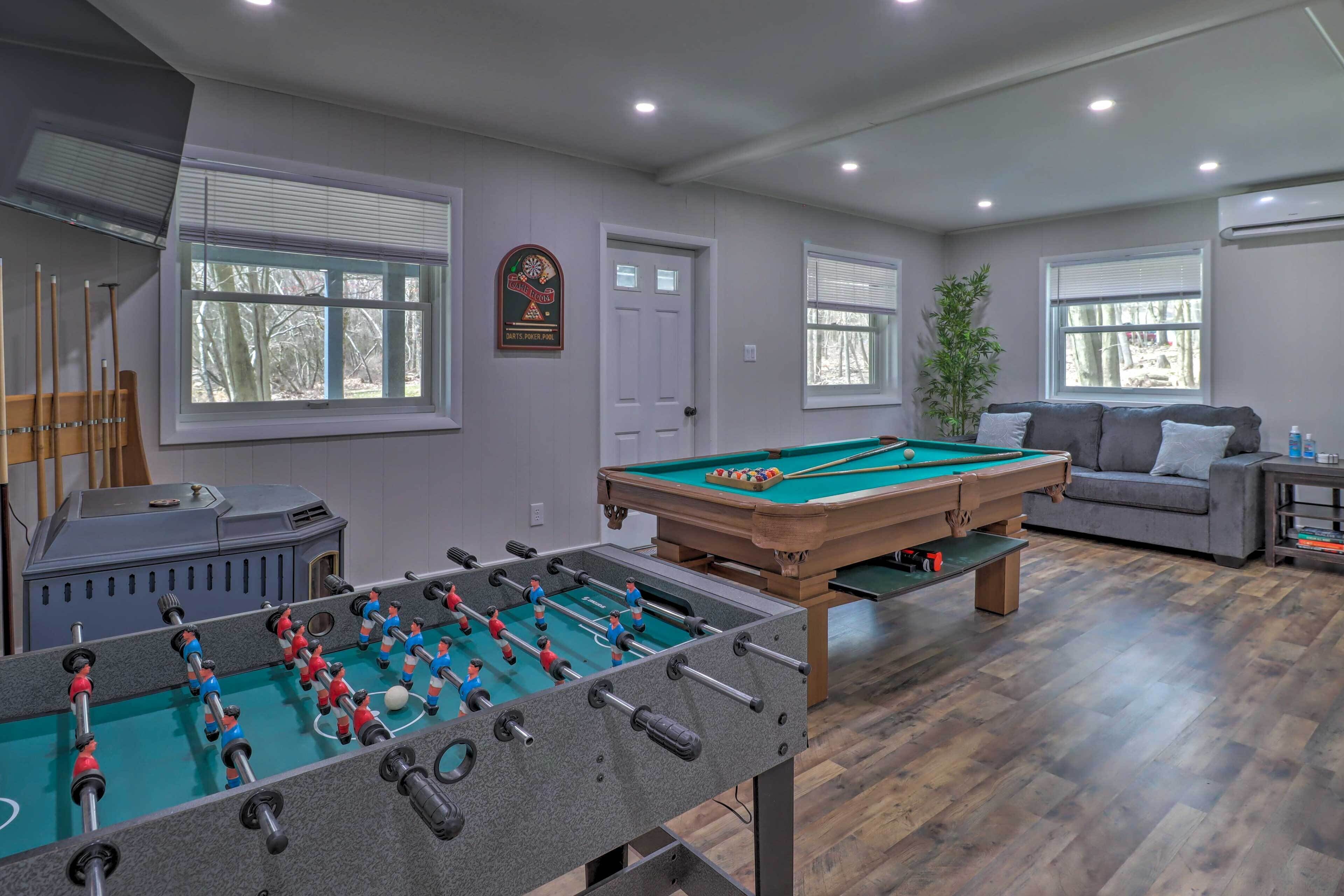 A room with a foosball table, a pool table, and a sofa.