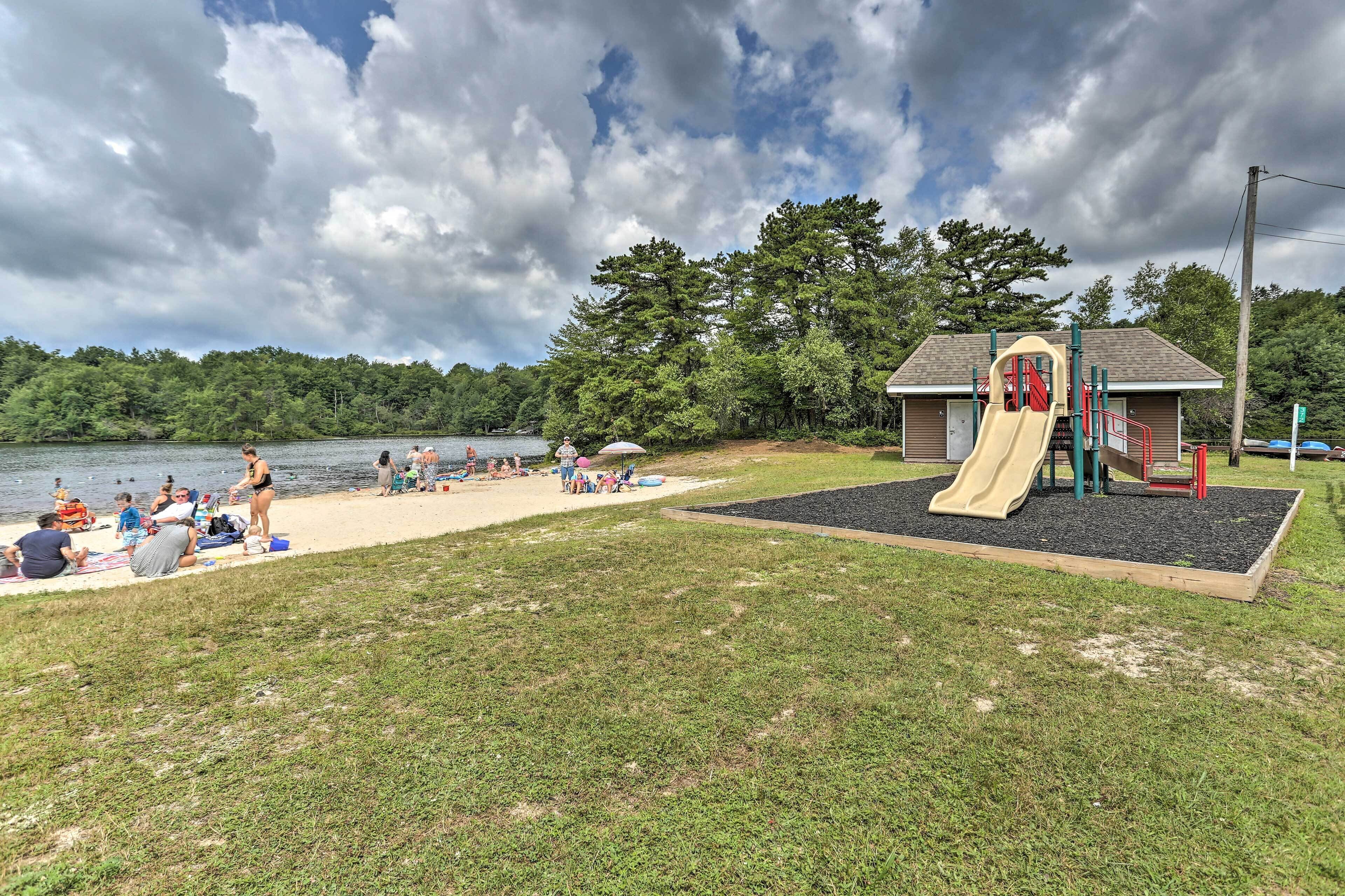 A playground with a slide and climbing structures, a sandy beach area, and a lake in the background.