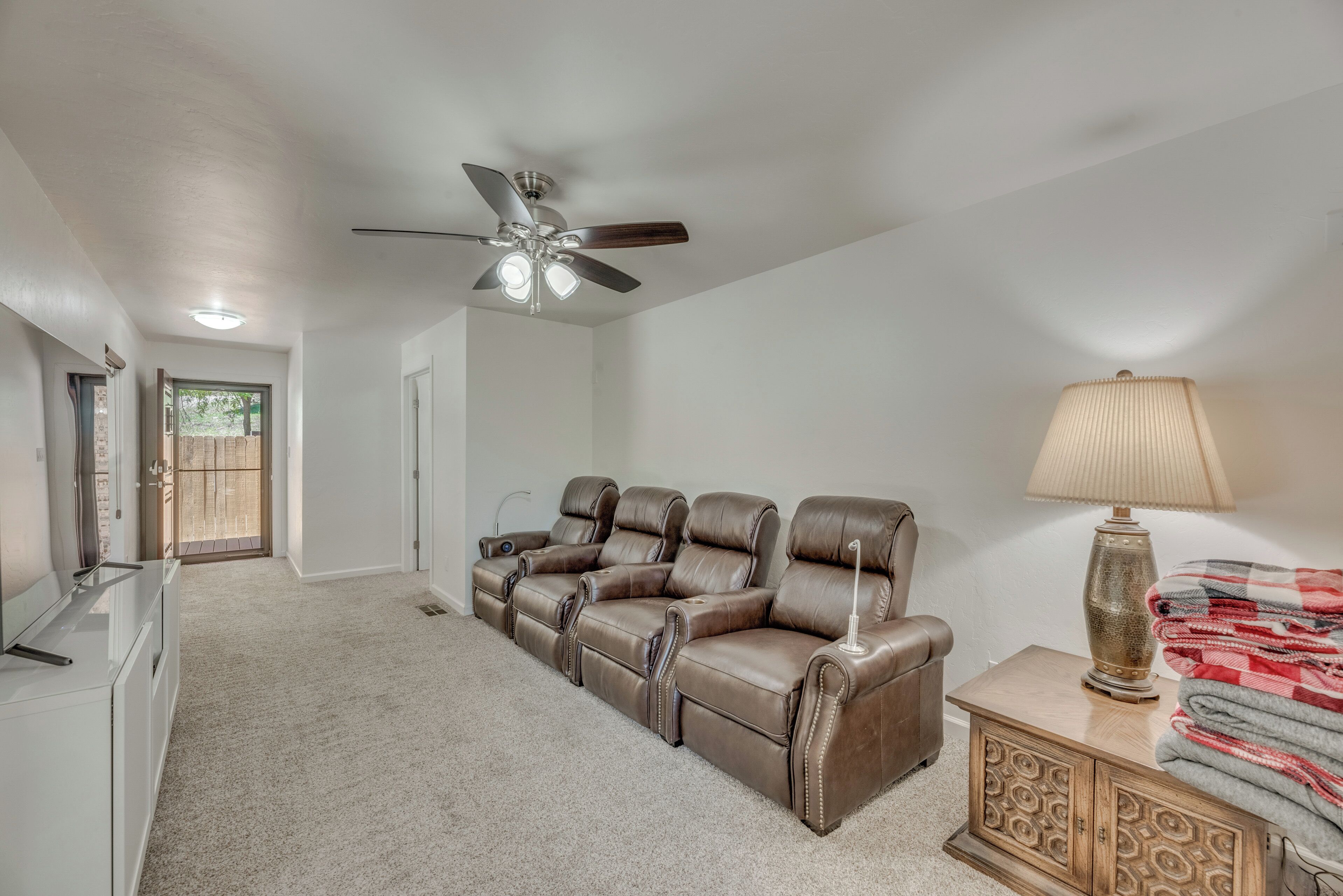 A spacious living room with a large sectional sofa, a ceiling fan, a lamp, and a cabinet with blankets.