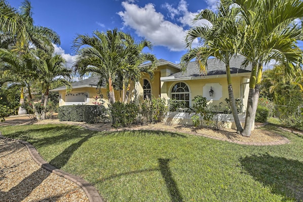 A yellow house with a well-maintained lawn and palm trees.