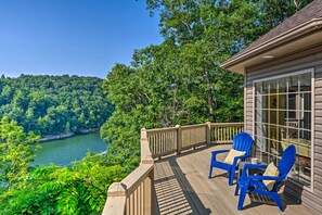 A wooden deck with blue chairs and a glass door, overlooking a river and forested area. - Luxe Lake Cumberland Retreat w/ Decks on 1 Acre! (Jamestown)
