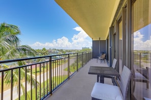A balcony with a view of a road and palm trees, a table with chairs, and a yellow awning.
