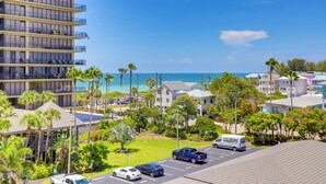 A multi-story hotel with balconies overlooking a beach, a parking area with several vehicles, and lush greenery.