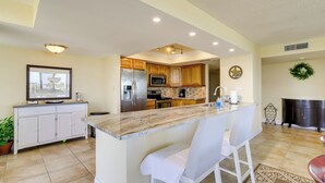 A modern kitchen with a central island, white bar stools, and a view of the dining area.