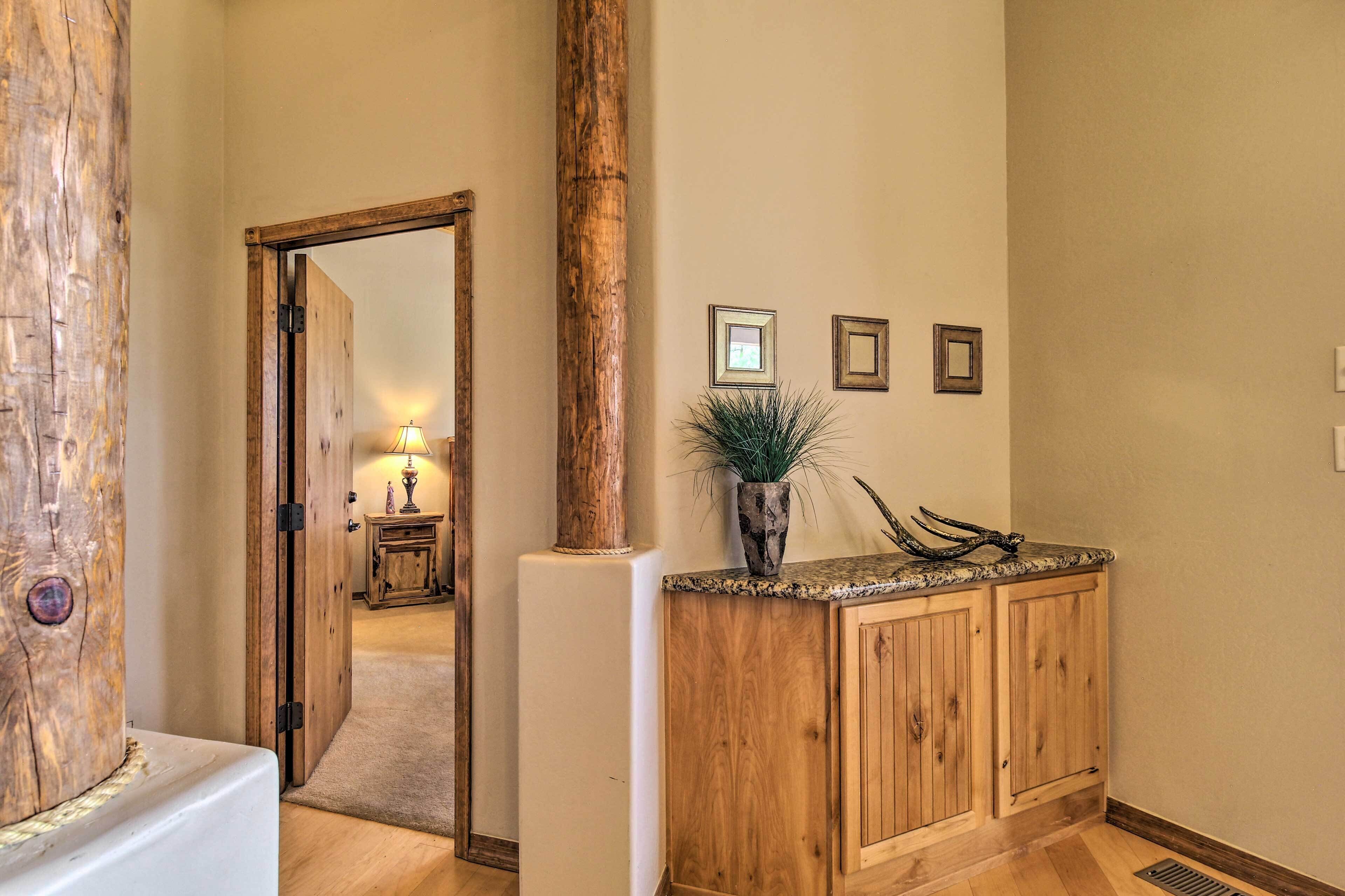 A hallway with a wooden door, a large wooden column, a potted plant, and a small table with a lamp.