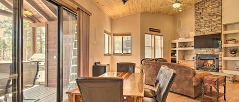 A spacious living area with a wooden ceiling, a fireplace, and a large window overlooking a deck.