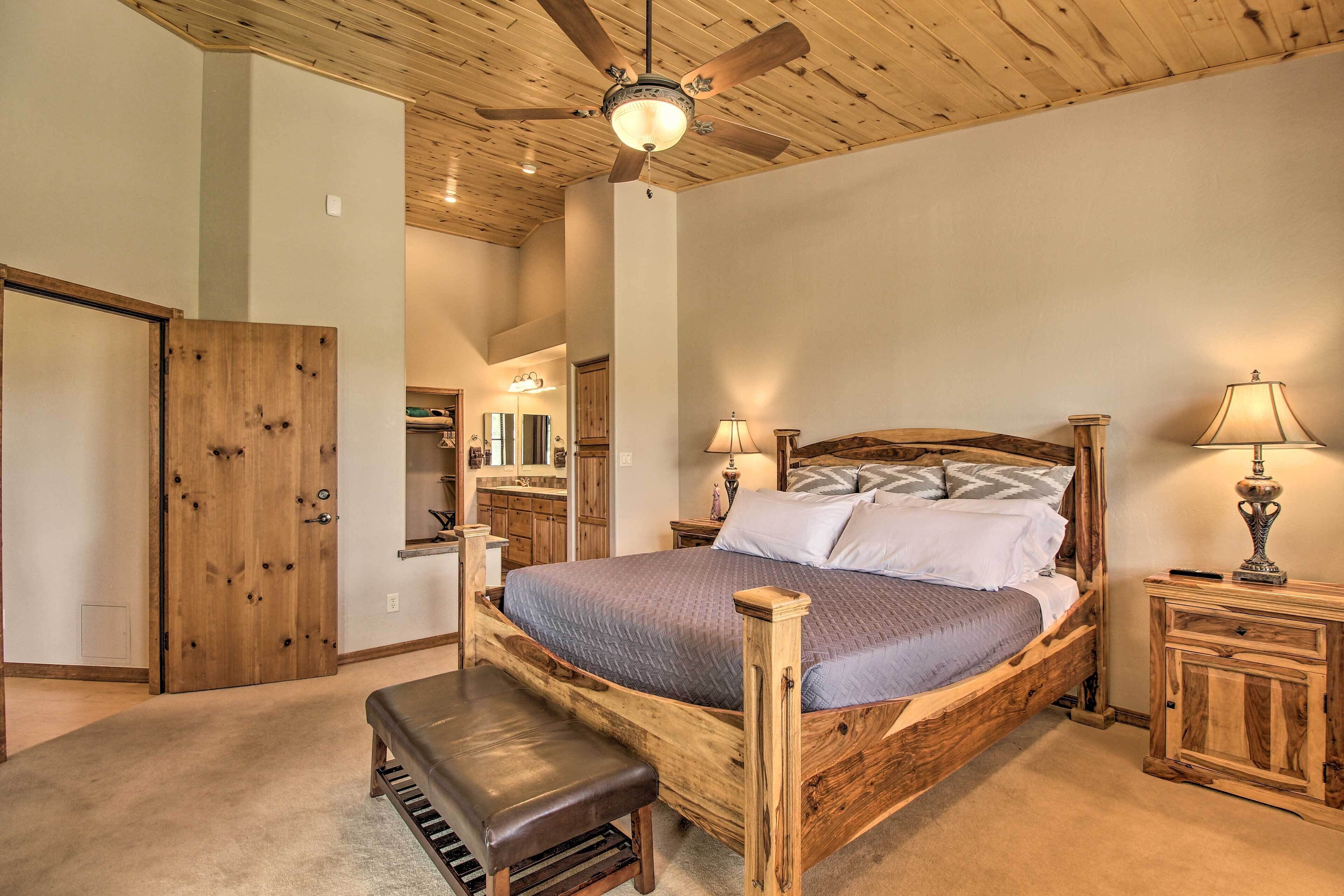 A bedroom with a wooden bed frame, a bench, a ceiling fan, and a nightstand with a lamp.