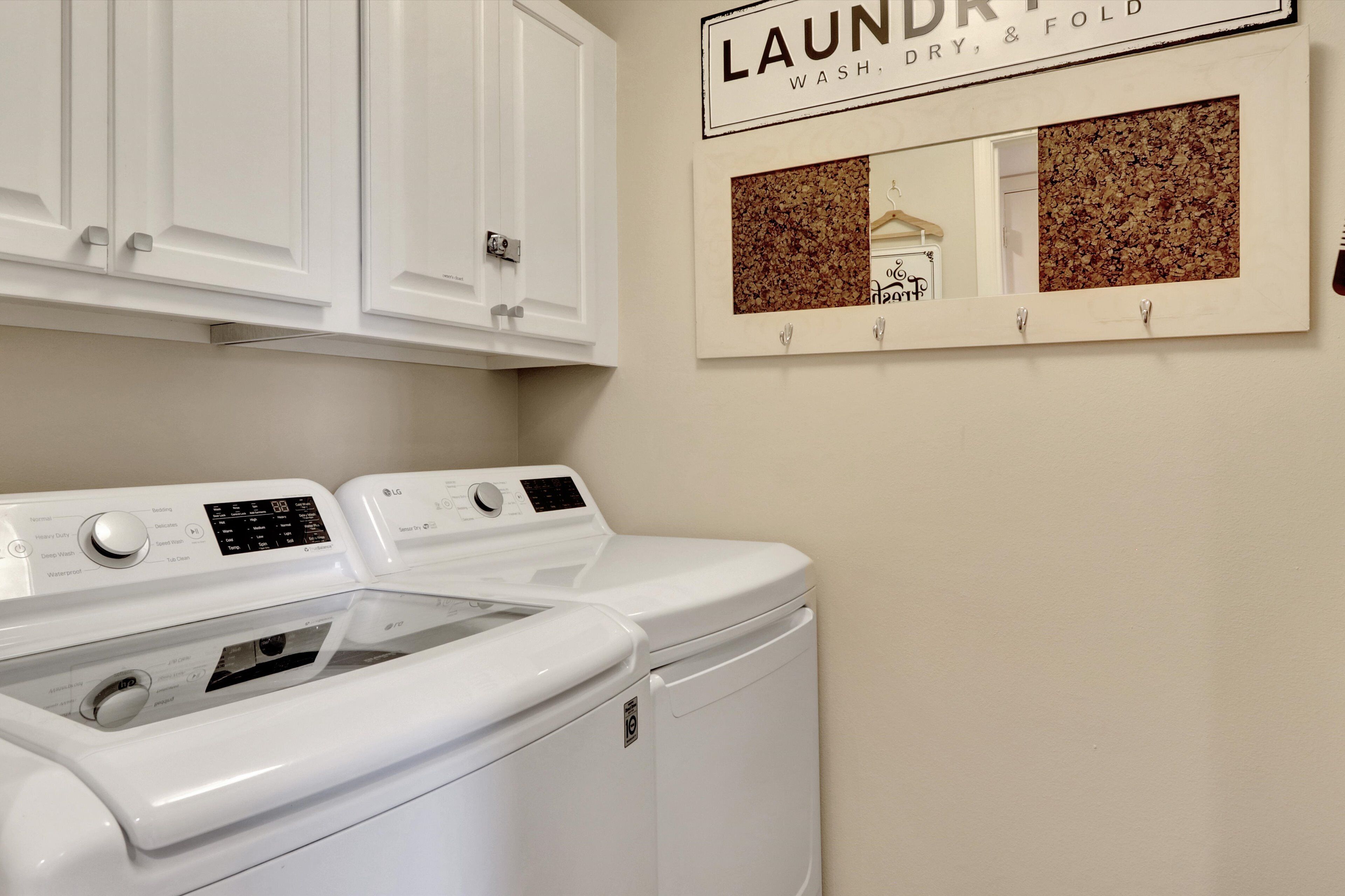 A laundry area with two white front-loading washers and dryers, a wall-mounted mirror, and a sign above reading "LAUNDRY, WASH, DRY, & FOLD".
