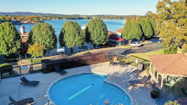 A swimming pool with lounge chairs, a deck area, and a view of a lake with trees and houses in the background. - Pool & Dock Access: Lakefront Hot Springs Condo! (Hot Springs)