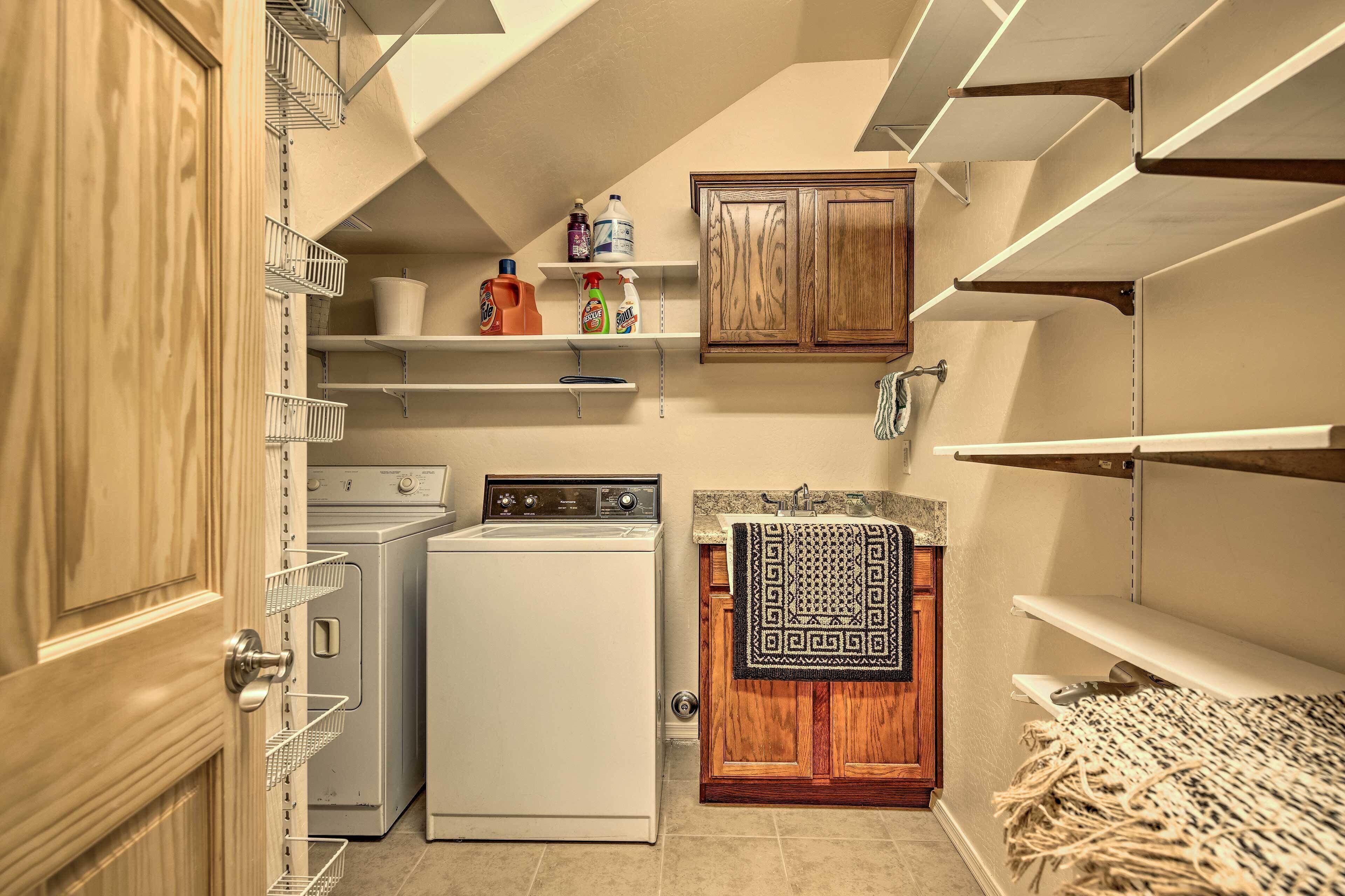 A laundry room with a washing machine, dryer, shelves with cleaning supplies, and a wooden cabinet.