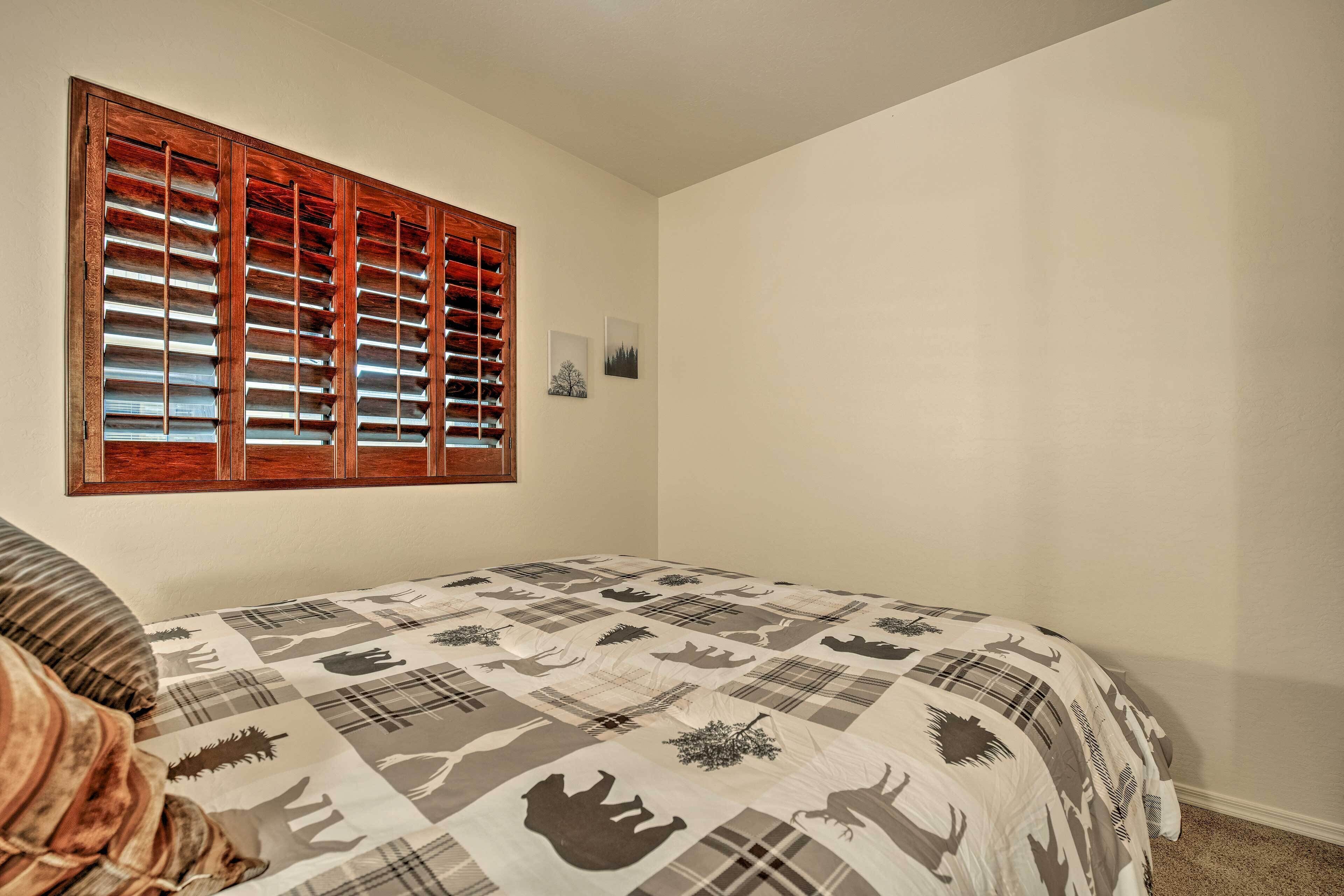 A bedroom with a large bed, a window with wooden blinds, and two framed pictures on the wall.
