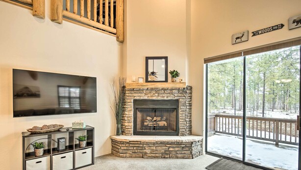 A living room with a stone fireplace, a large flat-screen TV, and a sliding glass door leading to a deck. - Deck & Game Room: Spacious Pinetop Cabin! (Pinetop)