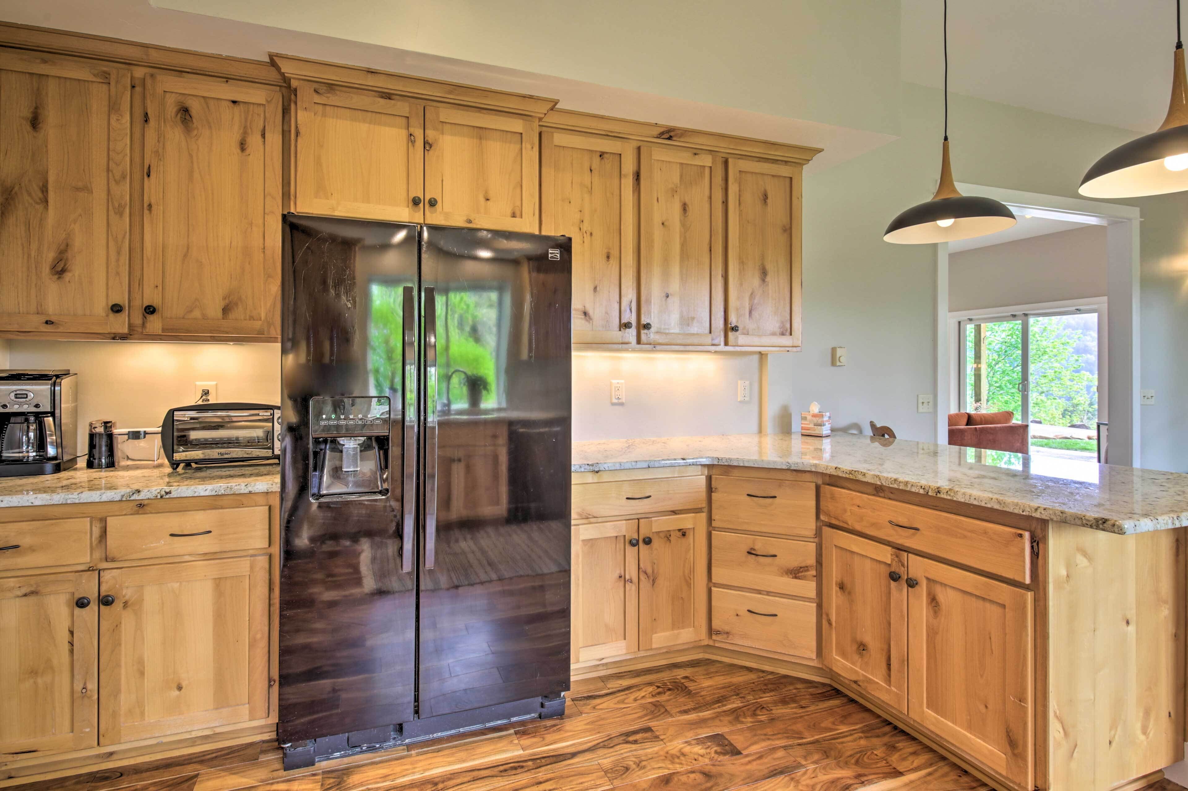 A kitchen with wooden cabinets, a stainless steel refrigerator, a water dispenser, and a granite countertop.