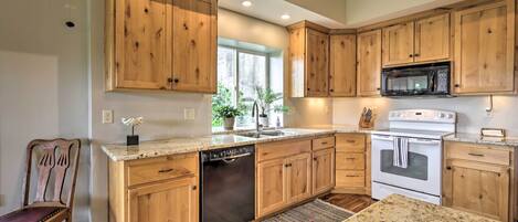 A kitchen with wooden cabinets, a dishwasher, a microwave, an oven, and a granite countertop.
