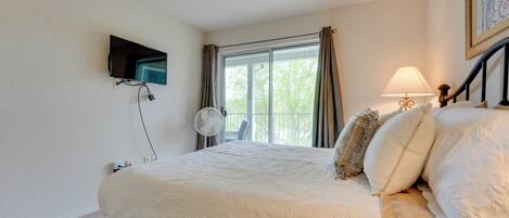 A bedroom with a bed, a TV mounted on the wall, a window with curtains, and a bedside lamp.