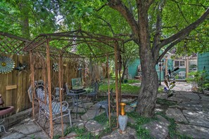 A rustic outdoor patio with a metal pergola, stone flooring, and various garden chairs and tables.