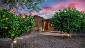 A modern house with a brick exterior, a red door, and a well-maintained garden with trees and shrubs. - Sun-lit Phoenix Gem: Backyard Entertainment Patio! (Phoenix)