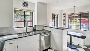 A modern kitchen with white cabinets, a black countertop, a dishwasher, and a window with a view of greenery. - Sun-lit Phoenix Gem: Backyard Entertainment Patio! (Phoenix)