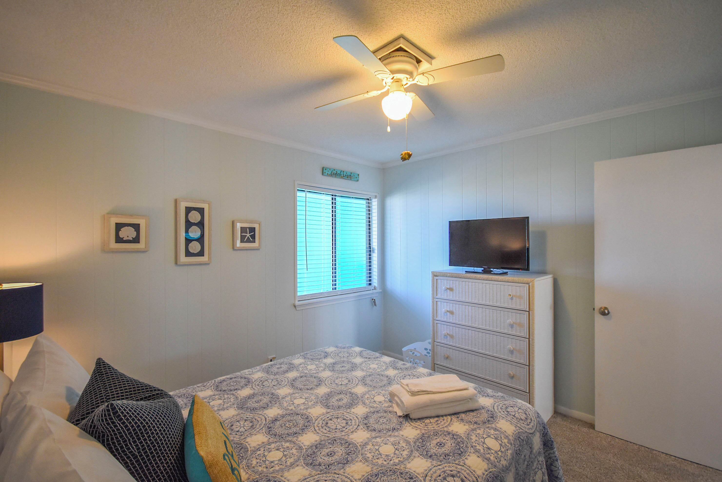 A bedroom with a bed, a dresser, a television, and a ceiling fan.