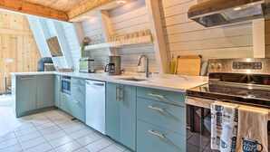 A modern kitchen with a built-in oven, a stovetop, and a sink. There are cabinets with gold handles and a countertop with various kitchen items. - Wilmington Chalet w/ Hot Tub < 8 Mi to Mount Snow! (Wilmington)
