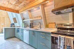 A modern kitchen with a built-in oven, a stovetop, and a sink. There are cabinets with gold handles and a countertop with various kitchen items. - Wilmington Chalet w/ Hot Tub < 8 Mi to Mount Snow! (Wilmington)