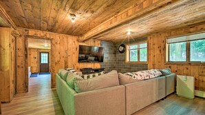 A cozy cabin interior with a wooden ceiling, a green sofa, a flat-screen TV, and a small refrigerator. - Wilmington Chalet w/ Hot Tub < 8 Mi to Mount Snow! (Wilmington)