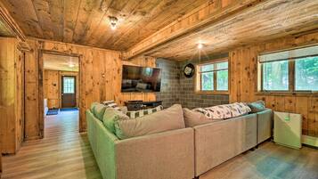 Interior acogedor de una cabaña con techo de madera, un sofá verde, un televisor de pantalla plana y un refrigerador pequeño.