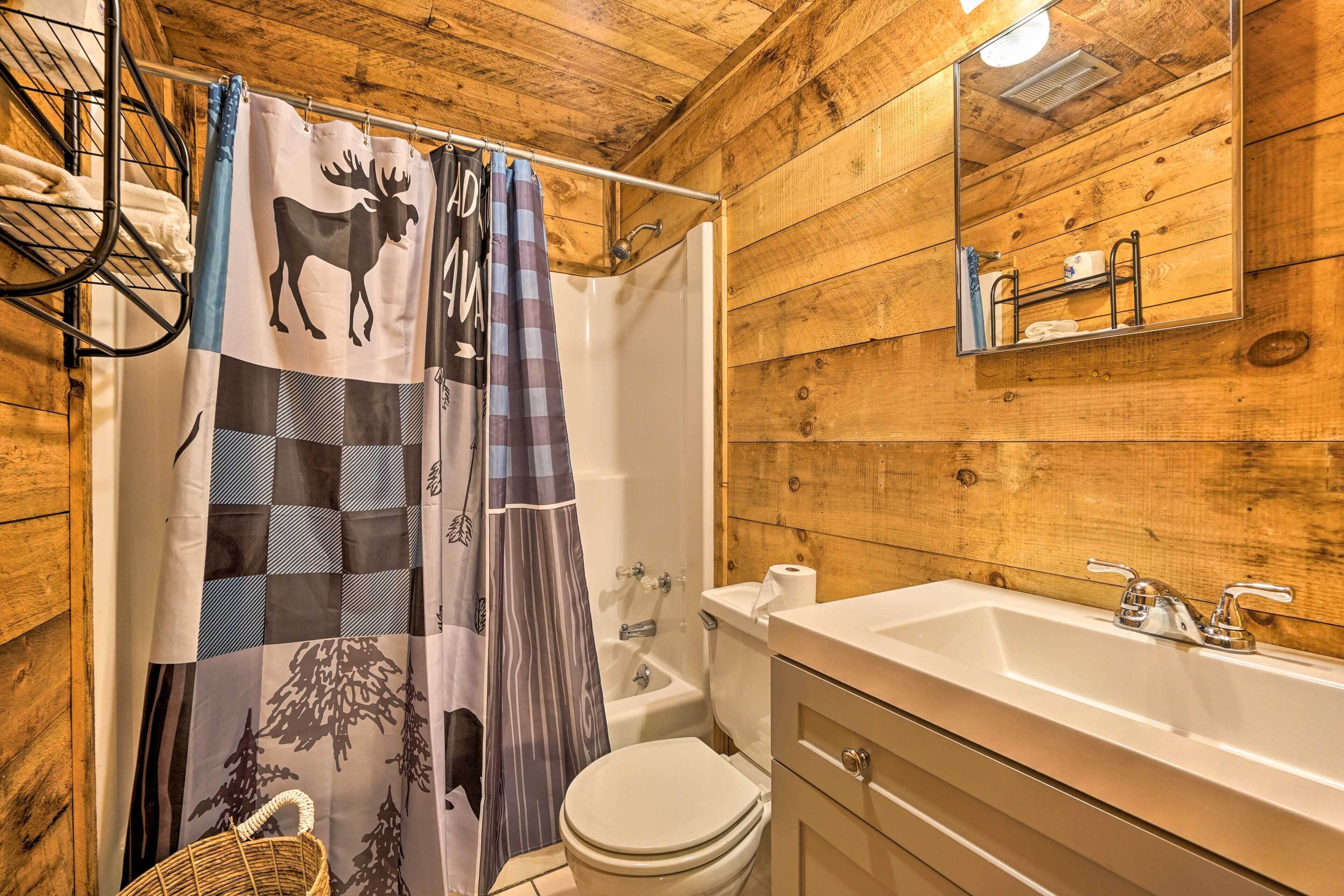 Une salle de bain avec des murs en bois, un lavabo blanc, des toilettes et un rideau de douche orné d’un motif d’élan.