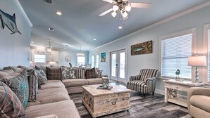A spacious living room with a large sectional sofa, a wooden coffee table, and a striped armchair. - Luxe Stilted Home w/ Kayaks: Walk to Beach (Dauphin Island)