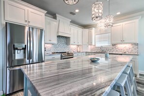 A modern kitchen with white cabinets, stainless steel appliances, a marble island, and pendant lighting. - Luxe Stilted Home w/ Kayaks: Walk to Beach (Dauphin Island)