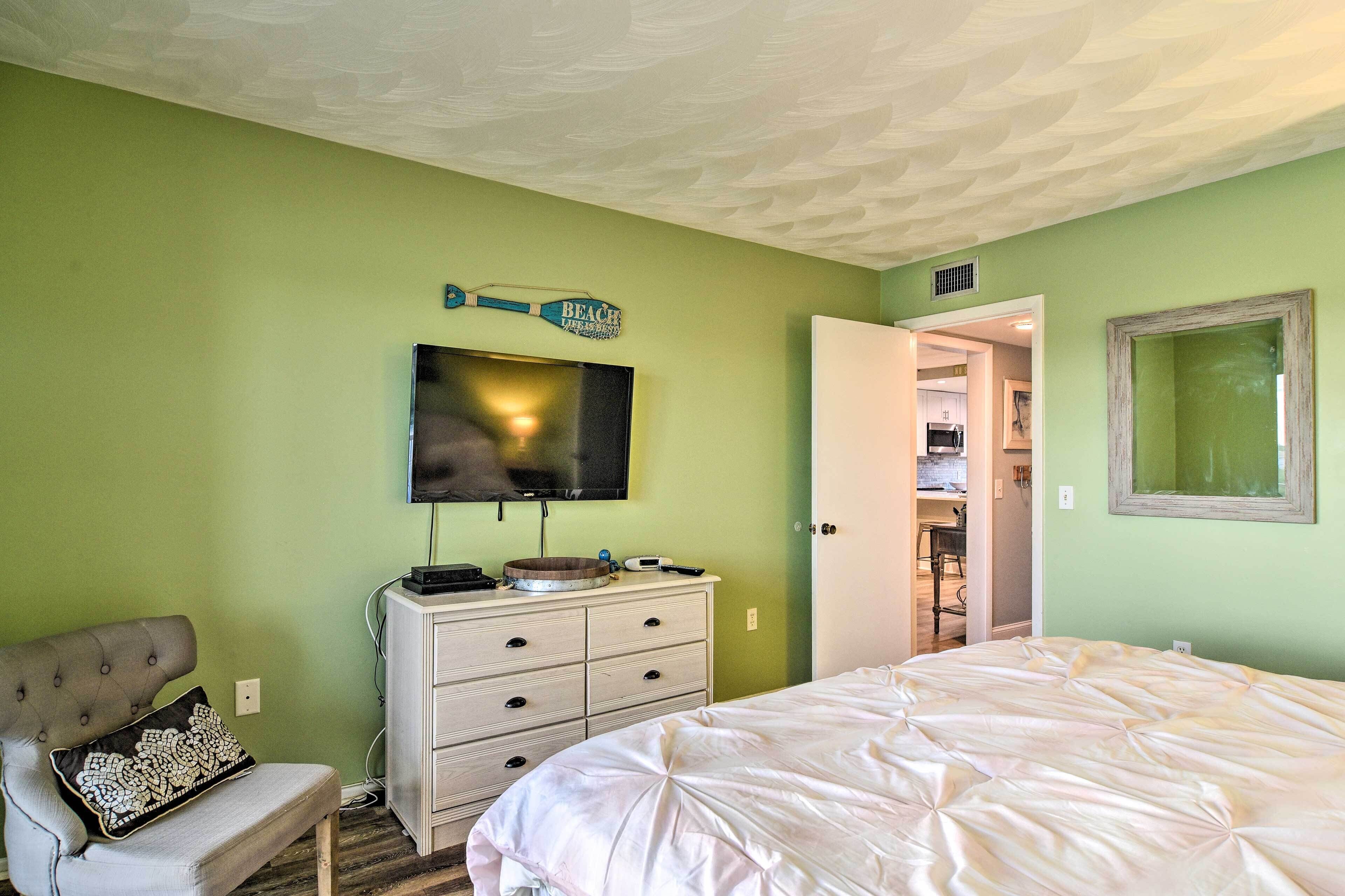 A bedroom with a bed, a dresser, a television, and a bench.