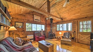 A cozy cabin interior with a wooden ceiling, a fireplace, a sofa, a coffee table, and a bookshelf. - Cozy Cottage on Cat Cove w/ Wraparound Deck! (Stonington)