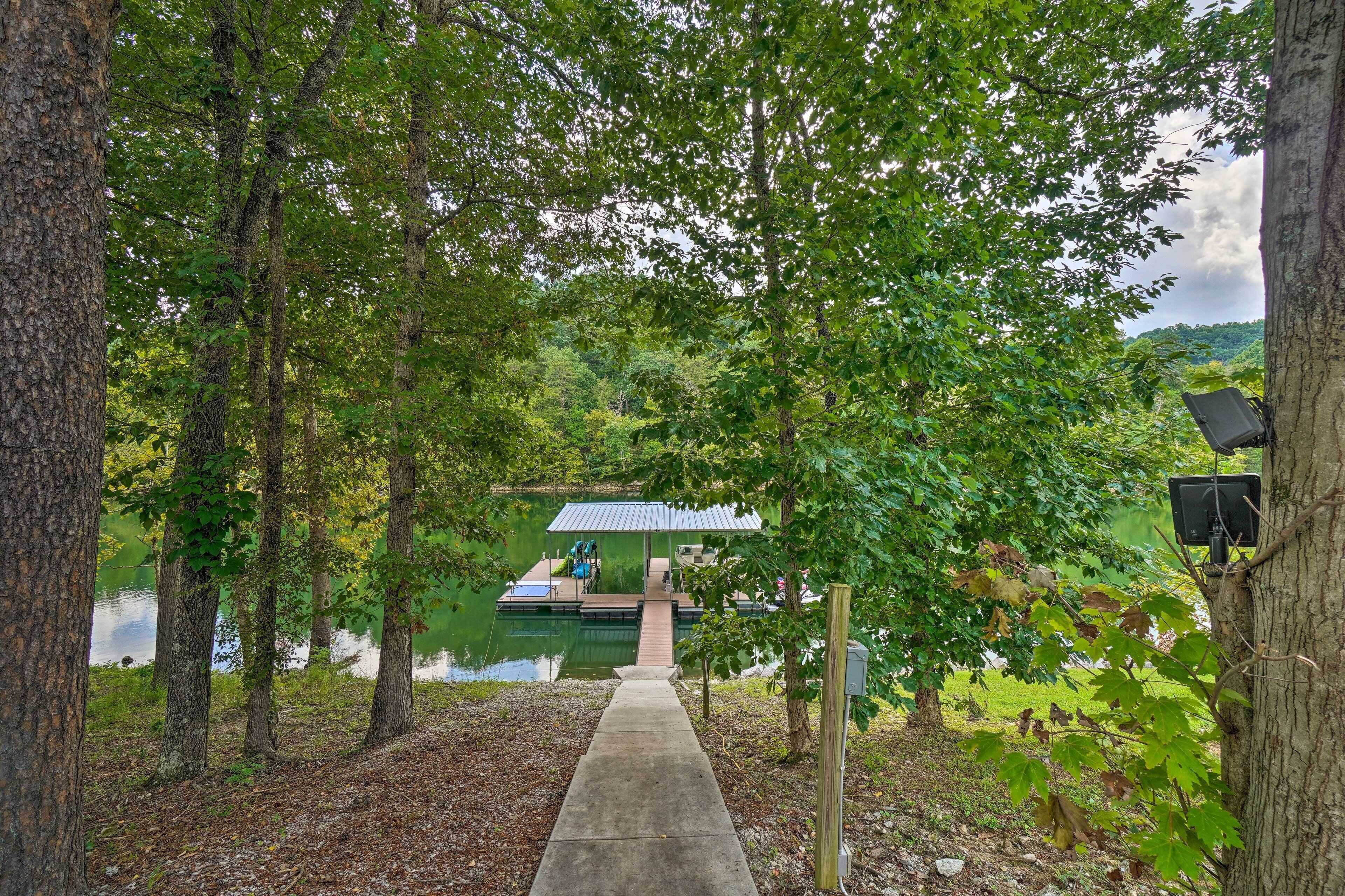 A concrete pathway leading to a dock with a small building, surrounded by trees and a lake.