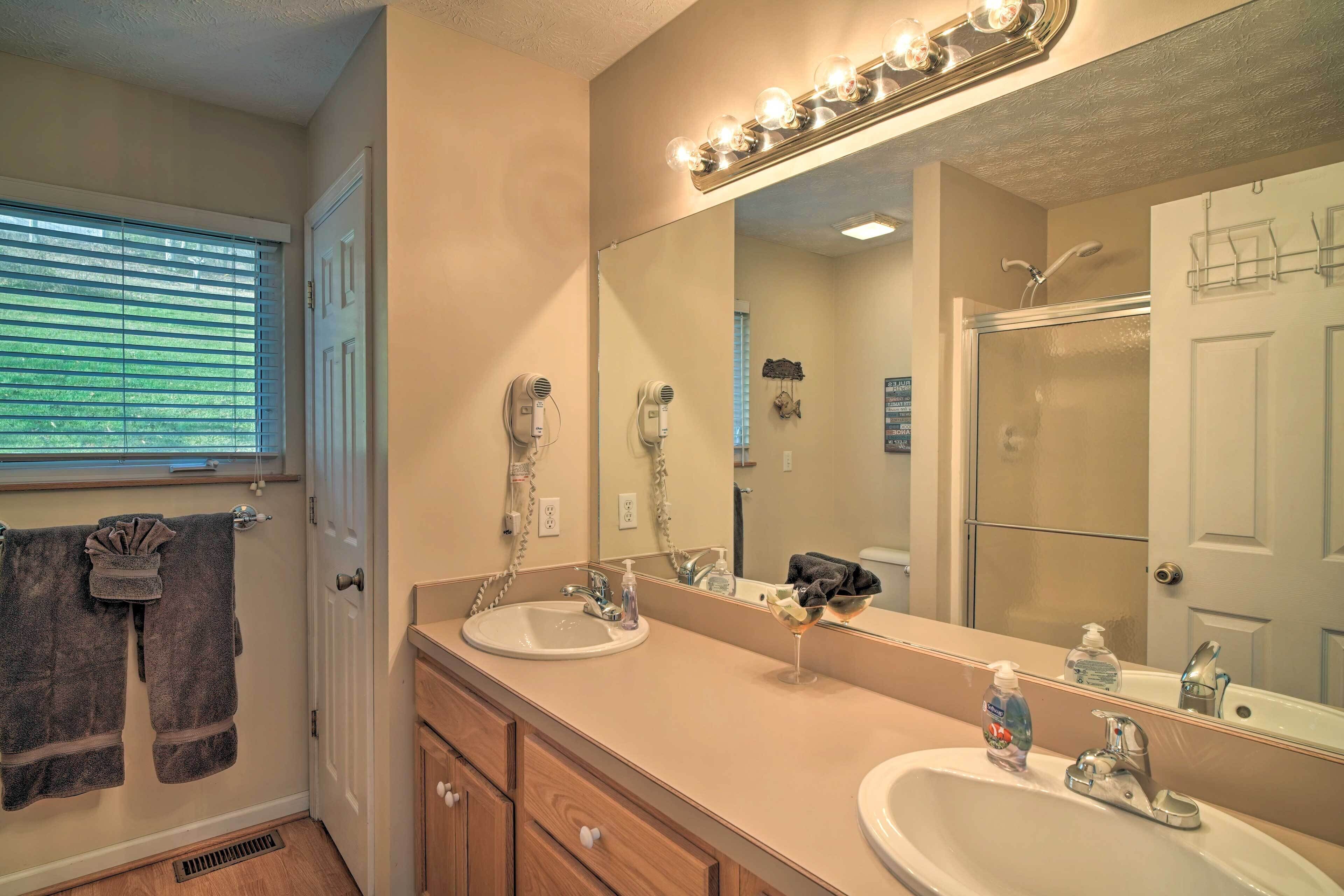A bathroom with two sinks, a large mirror with lights, a towel rack, and a shower.