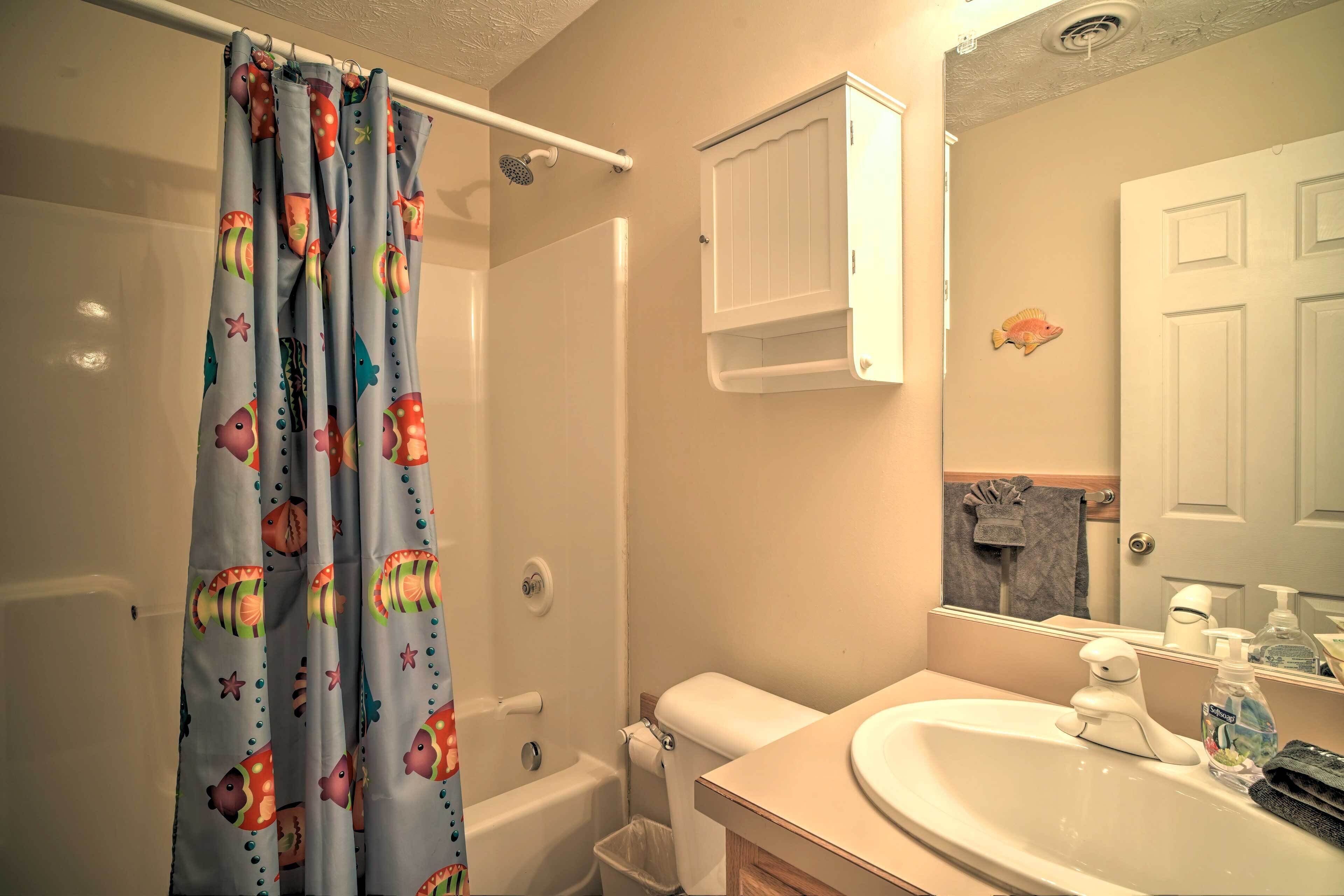 Un baño con cortina de ducha con motivos de peces, un inodoro, un lavabo con espejo y un armario sobre el lavabo.