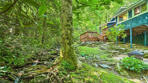 Une maison dotée d’une terrasse en bois et d’un sentier de pierres menant à une petite cascade.