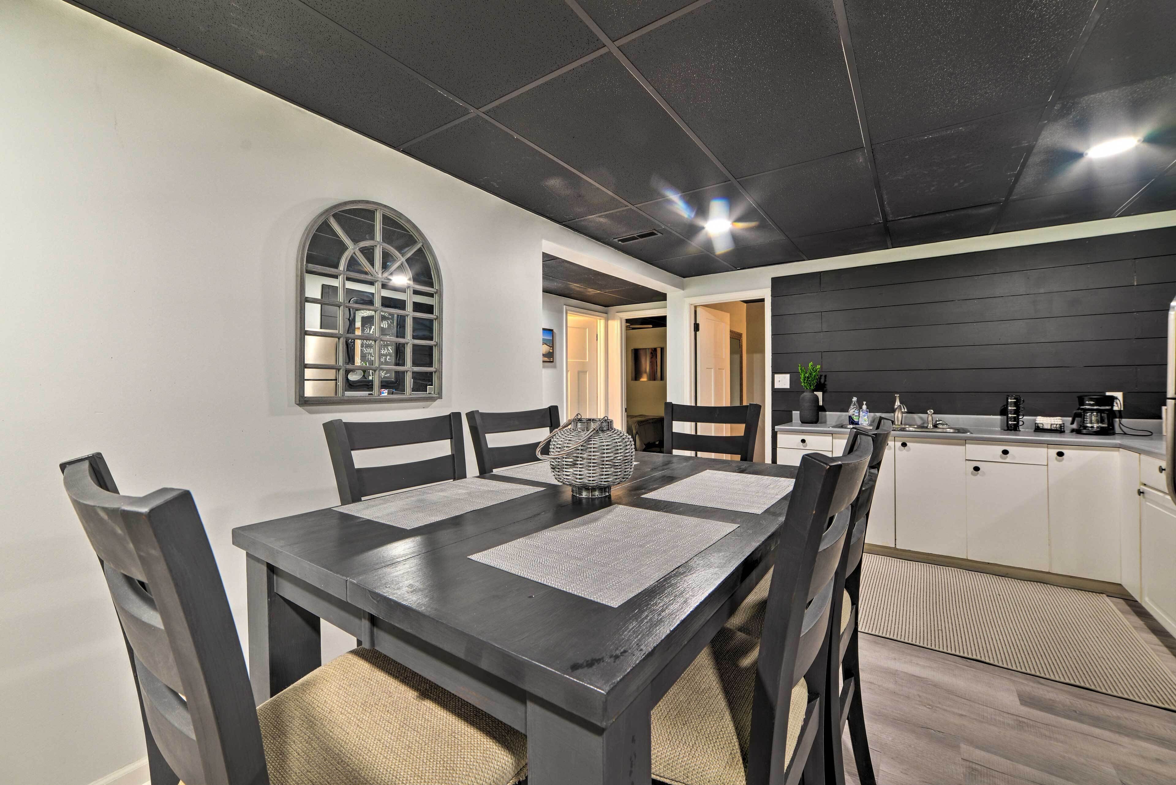Un coin repas avec une table et des chaises en bois foncé, ainsi qu’un élément décoratif central. Une fenêtre à motifs géométriques offre une vue sur l’intérieur.