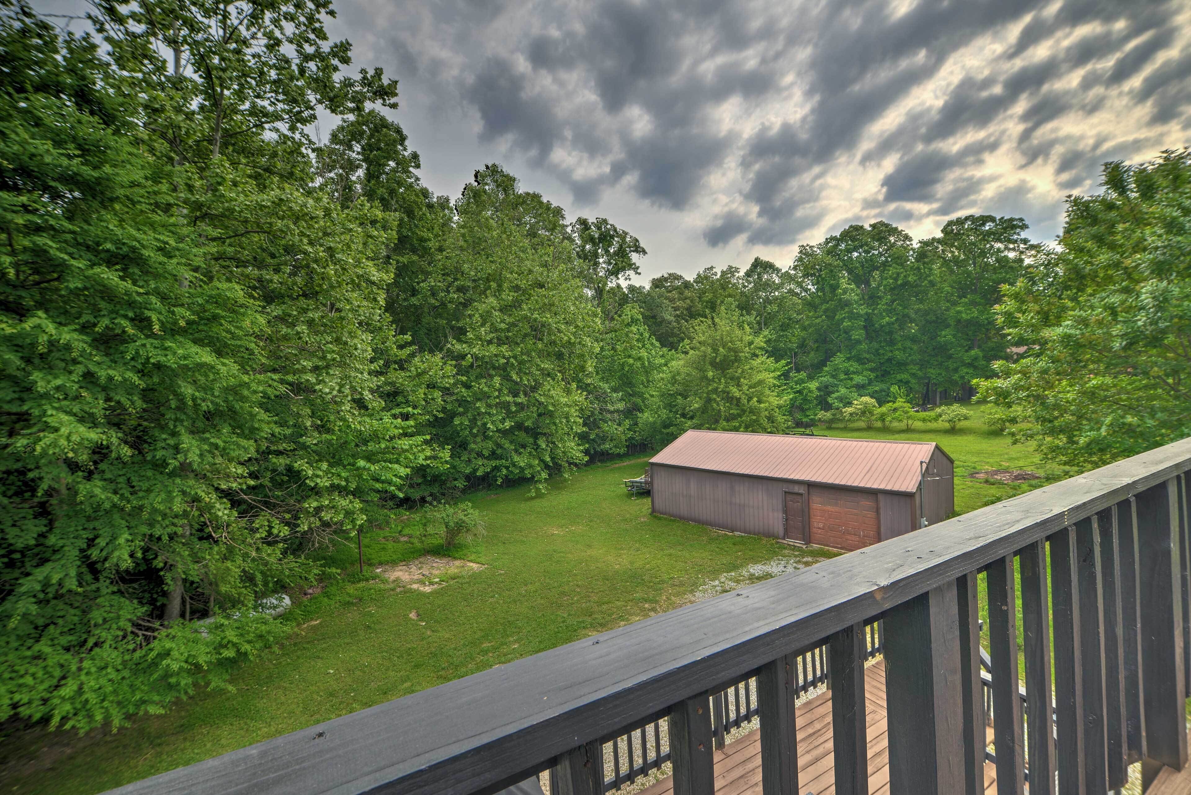 A view from a wooden deck overlooking a grassy yard with a red barn and dense trees.