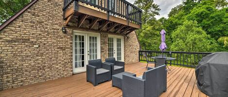 Una terraza de madera con mobiliario exterior, una zona de estar cubierta y un edificio de ladrillo con balcón.