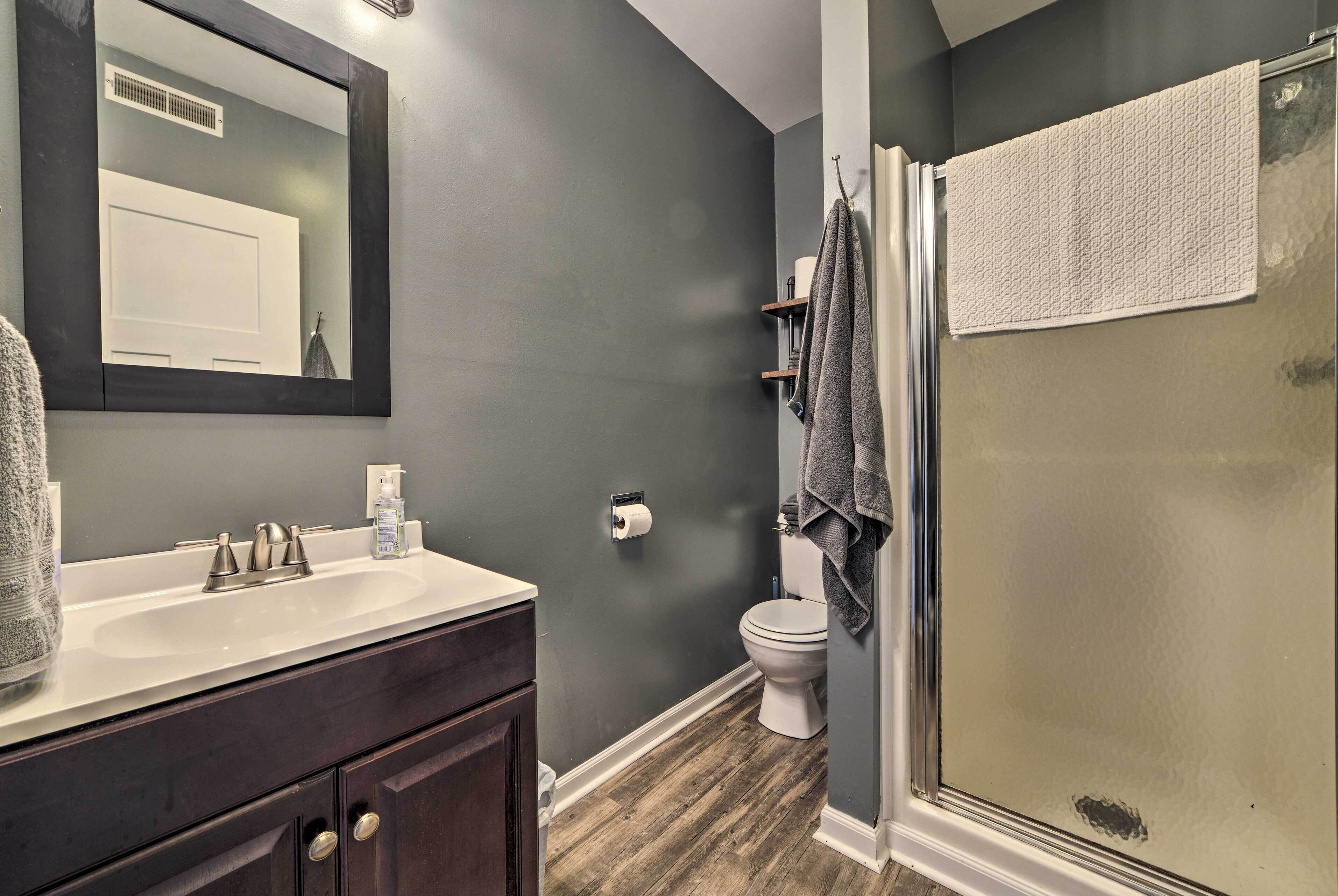 Une salle de bain avec un mur gris foncé, un lavabo blanc, un miroir, des toilettes et une cabine de douche en verre.